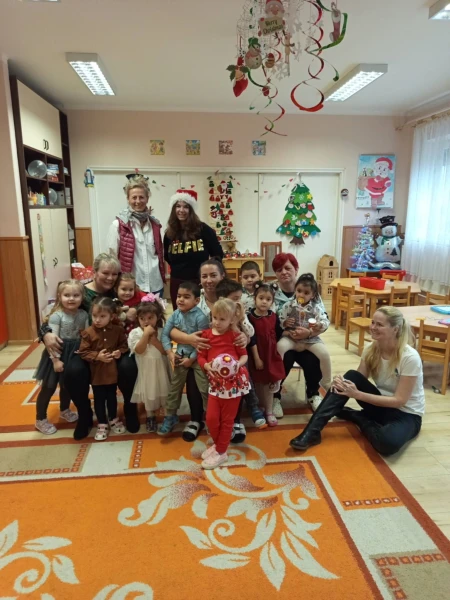 Gyerekek és felnőttek csoportképe egy karácsonyfával díszített teremben, néhányan mikulássapkában