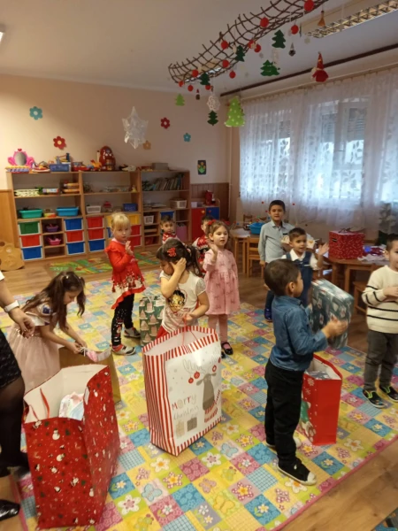Gyerekek ajándékzacskókkal egy karácsonyi díszekkel feldíszített teremben