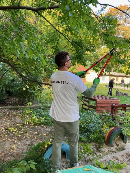 Egy önkéntes VOLUNTEER feliratú pólóban ágakat metsz egy játszóudvaron